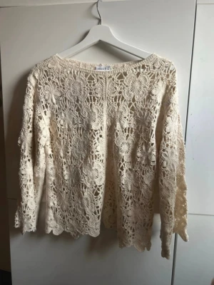 Beige virkad blommig tröja - Säljer en beige, långärmad virkad tröja med blommigt mönster. Tröjan har rund halsringning och är gjord i ett tunt, luftigt material som ger en bohemisk känsla. Perfekt för lager på lager och för dig som gillar unika detaljer.
