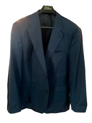Mörkblå klassisk kavaj  - Snygg mörkblå kavaj ifrån These Glory Days med två knappar framtill och klassiska slag. Kavajen har tre fickor på framsidan och är helfodrad för en stilren look. Passar perfekt till skjorta och jeans för en dressad stil. Storlek 56 (motsvarar XL). Kavajen är endast använd vid 1 tillfälle, framstår som helt ny utan defekter. 