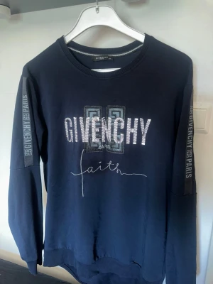 Svart Givenchy sweatshirt med tryck - Stilren svart sweatshirt från Givenchy med tryck på bröstet och texten 'faith' samt logga på ärmarna. Rund halsringning och långa ärmar. Perfekt för dig som gillar streetwear och exklusiva märken.