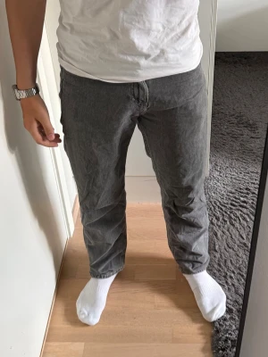 Grå raka jeans - Säljer ett par grå jeans med rak passform och klassisk femficksdesign. Jeansen har en enkel look utan slitningar eller dekorationer och är tillverkade i ett mjukt denimtyg. Perfekta för dig som gillar en clean och stilren stil.