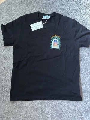Svart t shirt - Säljer en svart t-shirt med färgglatt tryck fram och stort grafiskt motiv på ryggen. T-shirten har korta ärmar, rund hals och är gjord i mjuk bomull. Perfekt för dig som gillar streetwear och vill sticka ut med snygg design.