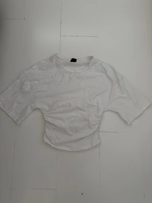 Vit t-shirt från Gina Tricot - En basic vit t-shirt från Gina Tricot i storlek XS. T-shirten har korta ärmar, rund halsringning och är gjord i mjuk bomull. Perfekt att styla med jeans eller kjol för en enkel och clean look.