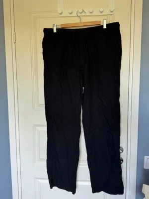 Svarta linnebyxor  - Säljer ett par svarta linnebyxor med avslappnad passform och elastisk midja med snörning. Perfekta för en chill och stilren look. Tillverkade i svalt linnematerial som passar bra till sommaren. Inga synliga loggor eller märken.