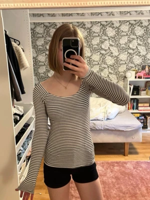 Randig slim tee tröja - Säljer en smalrandig topp i vitt och svart med lång ärm och bred, något fyrkantig ringning från Hollister. Modellen är slim tee, perfekt för en enkel men snygg look. Passar till både jeans och kjol.