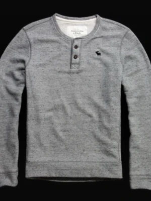  Abercrombie & Fitch Iconic Henley Swearshirt Size M - Snygg gråmelerad henleytröja från Abercrombie & Fitch med tre knappar vid halsen och diskret logobroderi på bröstet. Tröjan har långa ärmar och är tillverkad i mjukt bomullsmaterial. Perfekt för en avslappnad och stilren look.