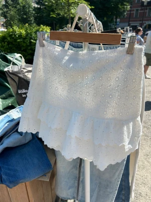 Vit volangkjol med broderi - Lågmidjad beroende på hur stor den är. Söt vit kortkjol med broderade blommor och volangkant. Kjolen har en romantisk känsla med fina detaljer och passar perfekt till sommaren. Tillverkad i bomull för en luftig och bekväm känsla.