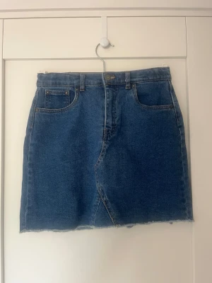 Blå jeanskjol från Levi's - Säljer en klassisk blå jeanskjol från Levi's med rå kant nertill och femficksmodell. Kjolen har normal passform och är tillverkad i slitstark bomull. Perfekt till sommaren och enkel att styla med olika toppar.