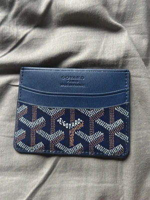 Blå korthållare - Snygg blå korthållare från med klassiskt mönster i vitt och brunt. Tillverkad i läder med flera kortfack och präglad logotyp framtill. Perfekt för dig som vill ha en stilren och exklusiv accessoar i fickan.