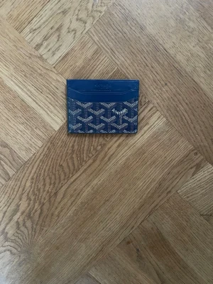 Blå kortfodral  - Snyggt blått kortfodral med deras klassiska mönster i vitt och grått. Fodralet har flera kortfack och är gjort i ett glansigt material som känns lyxigt och stilrent. Perfekt för dig som vill ha något smidigt och trendigt i fickan.