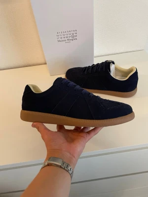 Masion margiela - Säljer ett par riktigt snygga Maison Margiela "Replica" German Army Trainers (GATs) i marinblå mocka med den klassiska gummisulan. Otroligt stilrena sneakers som passar till allt!  Märke: Maison Margiela (Paris)  Modell: Replica / GAT  Storlek: 42  Färg: Marinblå / Navy Blue  Skick: Helt nya och oanvända. Kommer i tillhörande skokartong. Riktigt fet färgkombination som är svår att få tag på. Detaljer som den klassiska Margiela-sömmen på hälen och "Replica"-taggen på insidan finns självklar