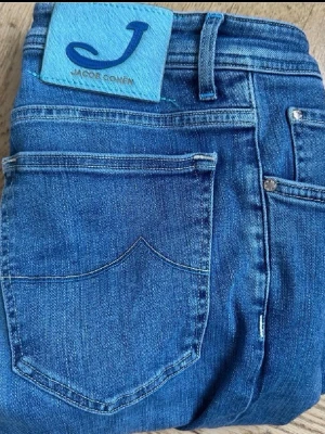 Blå jeans från Jacob Cohen - Säljer ett par klassiska blå jeans från Jacob Cohen. De har en rak passform, fem fickor och snygga kontrastsömmar. Jeansen är tillverkade i mjukt denimtyg och har en patch med logga bak i midjan. Perfekta till vardagslooken!