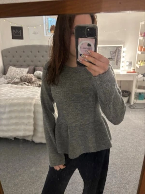Grå stickad tröja - Grå stickad tröja från H&M med peplumdetalj i midjan och rund hals. Tröjan har långa ärmar och är gjord i ett mjukt, fluffigt material som känns mjuk och skönt💞