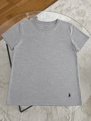 Ljusgrå t-shirt från Ralph Lauren - Snygg ljusgrå t-shirt från Ralph Lauren med klassisk passform och korta ärmar. Tillverkad i mjuk bomull och har den ikoniska lilla mörkblå loggan broderad nertill. Perfekt basplagg till garderoben.