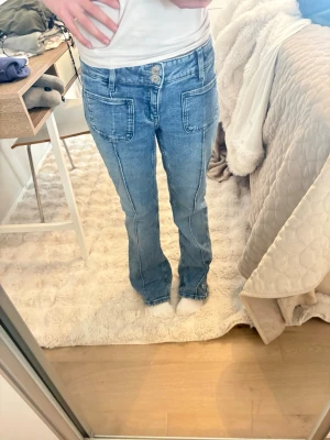 Blå jeans med stora fickor Gina Tricot - Snygga blå jeans från Gina Tricot med raka ben och stora framfickor. Jeansen har dubbla knappar i midjan och markerade sömmar som ger en cool retrovibe. Tillverkade i klassisk denim, perfekta för en avslappnad och trendig look.