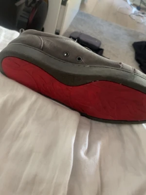 Gråa låga sneakers med röd sula - Snygga gråa sneakers i mockaliknande material med klassisk låg profil och snörning. Skorna har en unik röd yttersula som sticker ut och ger en cool kontrast till den neutrala ovandelen. Perfekta för dig som vill ha något stilrent men ändå vågat.