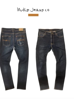 Mörkblå jeans från Nudie Jeans - Snygga mörkblå jeans från Nudie Jeans med klassisk femficksmodell och kontrastsömmar. Jeansen har smal passform och är tillverkade i mjuk denim med stretch. Bakfickorna har Nudie Jeans karakteristiska broderi.