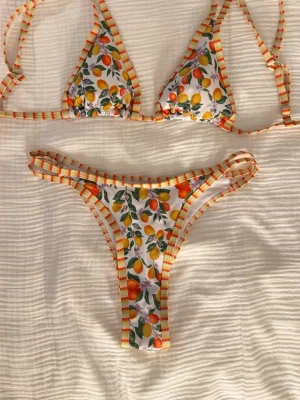 bikini med citrusmönster - Säljer en färgglad bikini med vita, gula och orange ränder samt citron- och apelsinmönster. Bikinin har trekantsöverdel med knyt i ryggen och justerbara axelband. Samt matchande underdel. Aldrig använd pågrund av att den tyvärr var för liten för mig. Perfekt för soliga dagar på stranden!