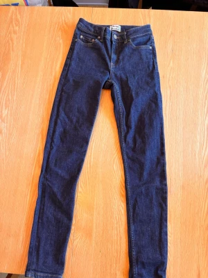 Mörkblå skinny jeans Acne Studios - Snygga mörkblå skinny jeans från Acne Studios med klassisk femficksdesign och guldfärgade sömmar. Jeansen har hög midja och är tillverkade i denim för en tight passform. Perfekta för dig som gillar stilrena och trendiga jeans.