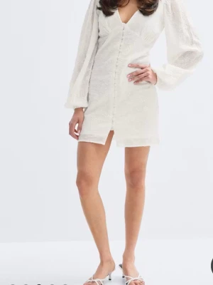 Gina tricot 14+ embroidery dress - Stilren vit kortklänning med v-ringad hals och långa puffärmar. Klänningen har knappar framtill och lätt struktur i tyget som ger en elegant känsla. Perfekt för dig som vill ha en chic och trendig look. Aldrig använt endast provat på säljer för att jag köpte fel strl och hann inte skicka tillbaka. Lapp är kvar på och ligger i påsen.