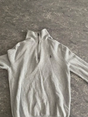 Polo Ralph Lauren - Snygg ljusgrå stickad tröja från Polo Ralph Lauren med halvzip och hög krage. Tillverkad i mjuk Pima Cotton