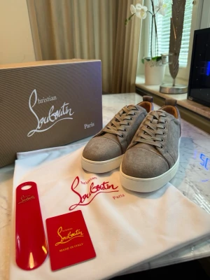 Gråa sneakers från Christian Louboutin - Stilrena gråa sneakers från Christian Louboutin med ovandel i mocka och vita, tjocka gummisulor. Skorna har klassisk låg profil, rund tå och matchande grå skosnören. Perfekta för dig som gillar exklusiva och trendiga sneakers.