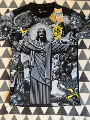 Nike Brasil grafisk fotbollströja M - Säljer en unik grafisk fotbollströja från Nike för Brasilien, storlek M. Tröjan har svart och grått mönster med Kristusstatyn, detaljer i gult och CBF-logga på bröstet. Tillverkad i lätt, tekniskt material med Dri-FIT för bästa komfort.