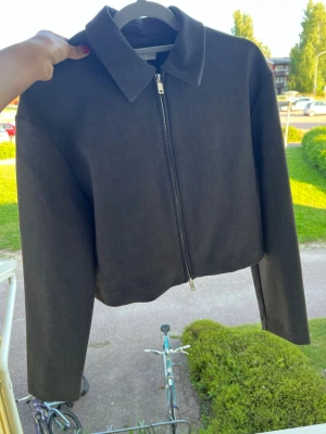 Mörkgrå croppad jacka med dragkedja - Snygg mörkgrå croppad jacka med klassisk krage och rak passform. Jackan har en hel dragkedja framtill och långa ärmar. Perfekt för dig som gillar minimalistisk stil och vill ha en enkel men trendig jacka till vardags.