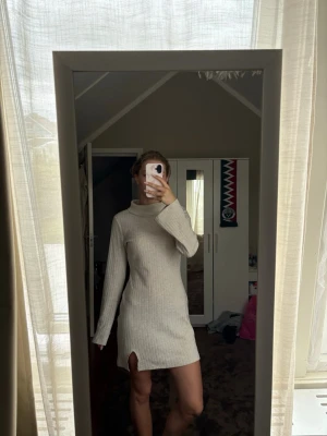 Beige ribbad poloklänning - Trendig beige kortklänning med polokrage och lång ärm. Klänningen är ribbad och har en liten slits framtill för extra stilpoäng. Perfekt för dig som gillar en enkel men snygg look.