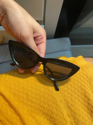 Svarta cat eye solglasögon - Snygga svarta solglasögon i klassisk cat eye-modell. Ramen är glansig och markerad, vilket ger en retro och trendig vibe. Perfekta för att lyfta vilken outfit som helst under soliga dagar.
