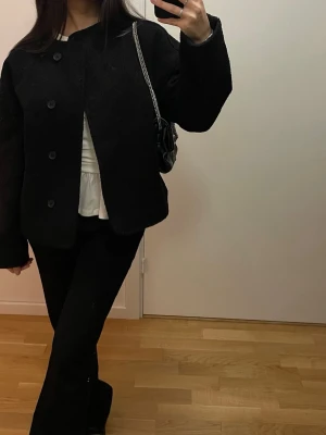 Svart teddyjacka med knappar - Säljer en svart teddyjacka med stora knappar framtill och avslappnad passform. Jackan har lång ärm och en mjuk, fluffig textur som ger en chill vibe. Perfekt att slänga på sig över en enkel outfit för en stilren look.