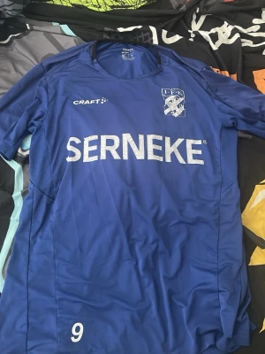 Blå IFK Göteborg matchtröja Craft - Säljer en blå IFK Göteborg matchtröja från Craft med vita tryck, klubbmärke på bröstet och sponsorlogga 'SERNEKE' framtill. Tröjan har nummer 9 och är tillverkad i ett lätt och ventilerande material, perfekt för fotbollsträning eller match.