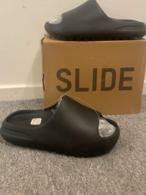 Svarta chunky slides tofflor - Säljer ett par svarta yeezy slides. Helt nya och aldrig använt. Storlek 43 men passar för er som har 44. LÅDAN INGÅR! Priset går att diskutera, skicka meddelande för mer bilder. 