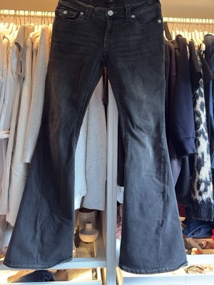 Svarta True Religion bootcut jeans med utsvängda ben - Säljer ett par svarta bootcut jeans med utsvängda ben och klassisk femficksmodell. Jeansen har vita detaljer på bakfickorna och silverfärgade knappar. Materialet är denim med lätt tvättad look för en cool vibe.