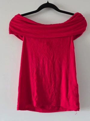 Röd offshoulder topp - Snygg röd offshoulder topp. Toppen är ärmlös och har en rak passform. Perfekt för dig som vill sticka ut med färg och stil.