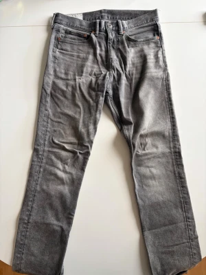 HM jeans - Säljer ett par grå jeans med tvättad look och raka ben. Klassisk femficksmodell med knappgylf och bälteshällor. Jeansen har en avslappnad passform och är tillverkade i denim, perfekt för en casual stil.