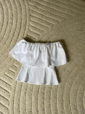 Vit volang tub topp - Säljer denna vita populära offshoulder topp med bred volang runt hela överdelen. Toppen är ärmlös och har en luftig, flowy passform som passar perfekt till fest. Lite rosa inuti (kolla sista bild)! Men absolut INGET man tänker på eller som syns när man har på sig den💗köpt för 500 på vinted. säljer för 300kr!