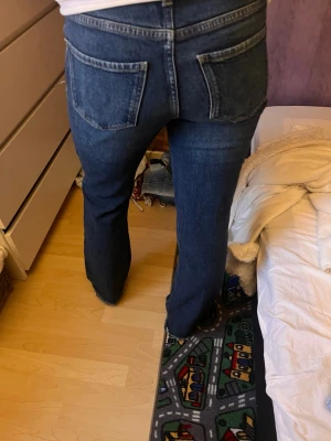 Mörkblå bootcut jeans med hög midja - Säljer ett par mörkblå jeans med bootcut-modell och mid midja. Jeansen har klassiska fem fickor, dragkedja och knapp framtill samt kontrastsömmar. Materialet är denim i bomull och passformen är figurnära upptill med utsvängda ben.