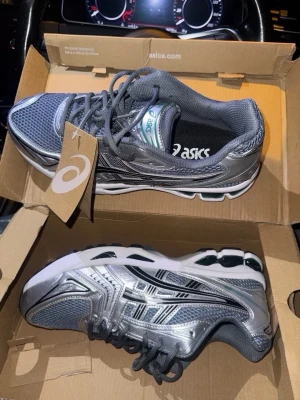 Asics silvriga sneakers - Säljer ett par riktigt snygga Asics sneakers i metallic silver med inslag av svart och vitt. Skorna har en sportig mesh- och syntetöverdel, klassisk Asics-logga på sidan och en chunky sula för extra komfort. Perfekta för dig som gillar retrovibbar och streetstyle. Är tillgänglig i alla storlekar 