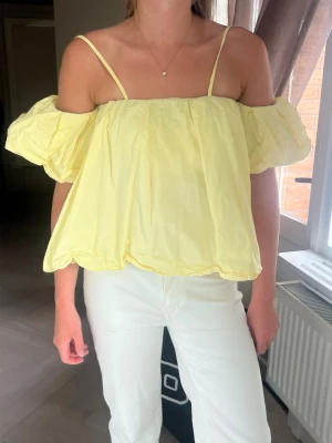 Ljusgul offshoulder topp med puffärm - Supersöt ljusgul topp med tunna axelband och puffiga offshoulder-ärmar. Luftig och flowy passform, perfekt för varma dagar. Tillverkad i ett lätt material som känns skönt mot huden. Matcha med jeans eller kjol för en fräsch look. Banden går lätt att vika ner! 