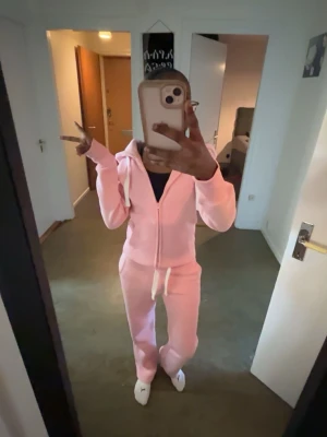 Rosa mjukisset från russemerch med dragkedja på hoodien! - Säljer ett par rosa mjukisbyxor i mjukt material med matchande hoodie - hoodien med storlek XXS och mjukisbyxorna med storlek XS! Byxorna har dragsko i midjan och raka ben. Hoodien har dragkedja, fickor och vit snörning i huvan. Perfekt för chill dagar eller när du vill vara extra bekväm och ha nått snyggt samtidigt!