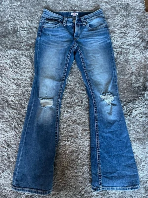 Lågmidjade bootcut jeans med slitningar - Snygga blå lågmidjade bootcut jeans med slitna detaljer och hål på knäna.  Storlek 170 men skulle säga att de sitter som S, är stretchiga i materialet. Säljer då de ej används. 