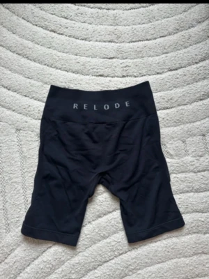 Svarta cykelshorts från Relode - Snygga svarta cykelshorts från Relode med hög midja och stretchigt material. Perfekta för träning eller en sportig look. Shortsen har en bred linning med logga framtill och sitter tight för en bekväm passform.