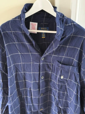 Polo Ralph Lauren Plaid Flannel Sleep Shirt  - Snygg mörkblå pyjamaströja från Polo Ralph Lauren med vitt rutmönster. Klassisk skjortmodell med knappar framtill och bröstficka med broderad logga. Säljes då den inte används, mycket gott skick. Priset kan diskuteras vid snabb och seriös affär! 
