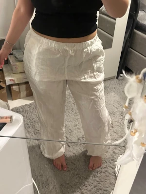 Vita linnebyxor - Säljer ett par vita linnebyxor med avslappnad passform och resår i midjan med dragsko. Byxorna har raka ben och är tillverkade i ett luftigt linnematerial, perfekta för en chill och stilren look.
