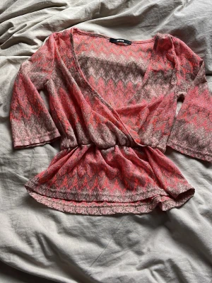 Omlottopp i neonrosa spets från Bik Bok - Säljer en snygg omlottopp från Bik Bok i neonrosa och beige spets. Toppen har trekvartsärm, v-ringning och elastisk midja som ger en smickrande passform. 