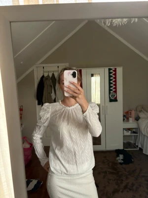 Vit blus med puffärmar - Stilren vit blus med puffiga axlar och långärmad design. Blusen har ett subtilt mönster i tyget som ger en lyxig känsla och rundad halsringning. Perfekt att matcha med både kjol och byxor för en trendig look.