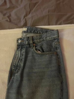 Blå baggy jeans med hög midja - Säljer ett par klassiska blå jeans med rak passform och hög midja. Jeansen har fem fickor, bälteshällor och stängs med knapp och dragkedja. Materialet är kraftig denim i bomull. Perfekta till en avslappnad stil. Är i storlek 40 men sitter mer som en 38.