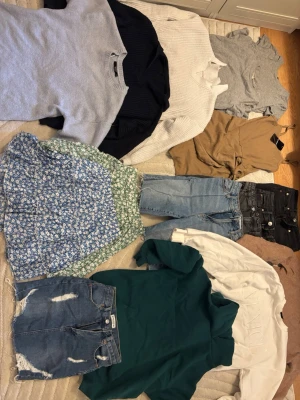 Stort klädpaket med blandade plagg - Säljer ett stort klädpaket med blandade plagg som stickade tröjor, jeans, kjolar, shorts, t-shirts, blusar och linnen. Färgerna varierar mellan blått, grönt, vitt, svart, beige och rosa. Materialen är blandade, bland annat denim, bomull och stickat. Perfekt för dig som vill uppdatera garderoben!