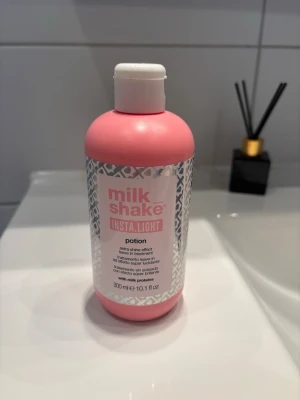 milk_shake Insta.Light potion 300 ml - milk_shake Insta.Light potion är en hårprodukt i en rosa plastflaska med vitt lock. Produkten ger extra glans och innehåller mjölkprotein. Flaskan rymmer 300 ml och har en modern, stilren design med silvermönster på etiketten. Öppnad men oanvänd 