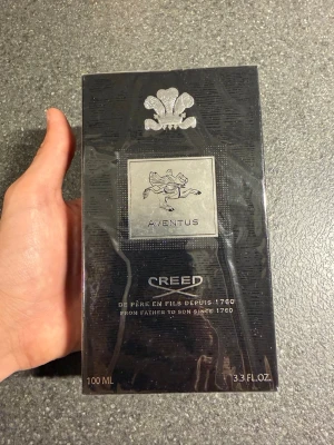 Creed Aventus Eau de Parfum 100ml - Lyxig parfym från Creed, Aventus, i en elegant svart förpackning med silverdetaljer och klassisk logotyp. Flaskan rymmer 100 ml och doften är känd för sin exklusiva och tidlösa karaktär. Perfekt för dig som vill ha något unikt och sofistikerat.
